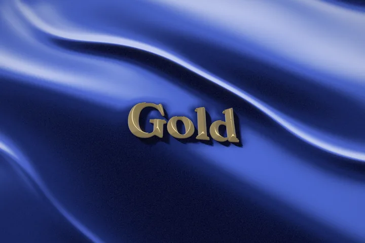The word Gold pressed into a deep blue velvet drape as raised gold letters, with pale light running along the folds of the fabric.